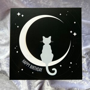 ゴシックな魔女の猫、月、星のバースデーカード | 明るい幾何学模様の背景を持つ暗くスピリチュアルなデザイン