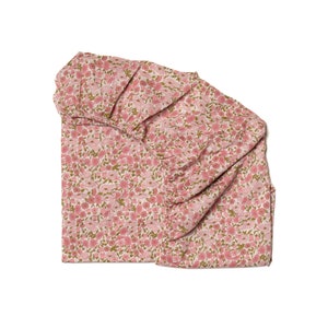 Peut inclure: Un tissu imprimé de fleurs roses et vertes avec un col à volants. Le tissu est froncé et drapé, créant un aspect doux et fluide.