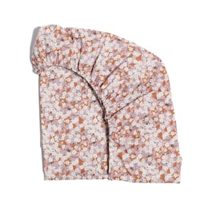 May include: A fitted sheet with a floral pattern. The sheet features a repeating design of small white and brown flowers on a light purple background. The edges are gathered, and the sheet is made of a soft fabric.