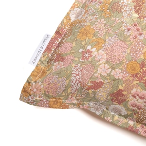 May include: Close-up of a pillow with a floral pattern in shades of yellow, pink, and green. The fabric features a dense arrangement of flowers and foliage. The tag reads "Poppy & Honesty".