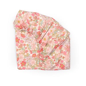 May include: A floral patterned fabric with a variety of pink flowers, green leaves, and a cream background. The fabric is folded over, showing the pattern and texture. The overall theme is a floral design.