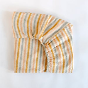 May include: A fitted sheet with a striped pattern in shades of blue, yellow, and pink. The sheet is made of a soft, natural fabric and is perfect for adding a touch of colour and style to any bedroom.