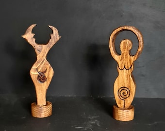 May include: Two wooden figurines, one depicting a woman with a circle above her head and a spiral in her belly, the other depicting a woman with a crescent moon and a star in her belly.
