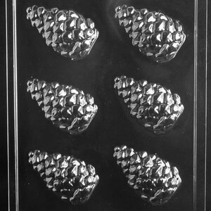 May include: A clear plastic mold with six cavities shaped like pine cones. The mold is designed for making chocolate or candy pine cones.