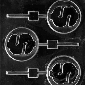 May include: A clear plastic mold for making candy lollipops. The mold has three cavities, each shaped like a dollar sign. The mold is designed to create lollipops with a stick.