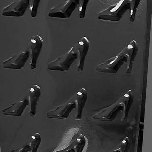 May include: A collection of black high-heeled shoes arranged in a grid pattern. The shoes have a classic design with pointed toes and stiletto heels. The image is in grayscale, highlighting the shape and form of the footwear.
