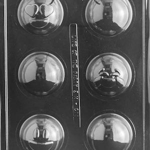 May include: A black plastic mold with six round cavities for making chocolate or candy. Each cavity has a different emoji face design, including a heart-eyed face, a smiling face, a crying face, and a blank face.