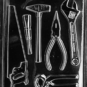 May include: A black and white mold for making chocolate tools. The mold includes a hammer, saw, pliers, wrench, and a pair of tongs. The mold is made of plastic and has a smooth surface. The text "LIFE ON THE FARM # 08823 FDA  ART D GC" is printed on the bottom of the mold.