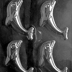 Puede incluir: Un molde para hacer formas de delfines de chocolate. El molde está hecho de plástico transparente y tiene cuatro cavidades de delfines.