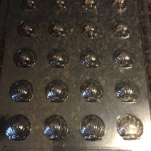 Puede incluir: Un molde de plástico negro con 16 cavidades individuales con forma de conchas. El molde está etiquetado como "East Coast Molds Co."