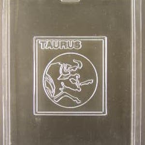 May include: A clear plastic mold for making chocolate or candy. The mold is shaped like a square with a circle inside. The circle has a design of a bull, the astrological symbol for Taurus. The text "TAURUS" is printed above the bull.