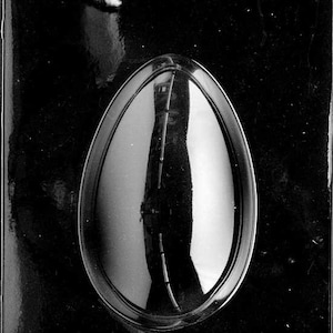 Może przedstawiać: Czarna plastikowa forma do robienia czekoladowych jajek. Forma ma jedną wnękę w kształcie jajka.