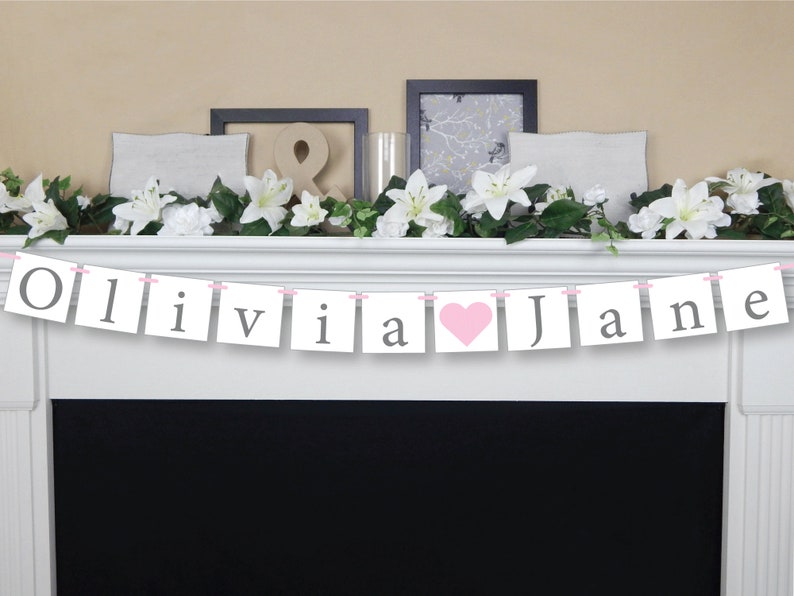 May include: A white banner with pink string and gray letters spelling "Olivia & Jane" with a pink heart between the names.