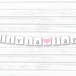 May include: A white banner with pink string and gray letters spelling "Olivia" with a pink heart and "Jane".