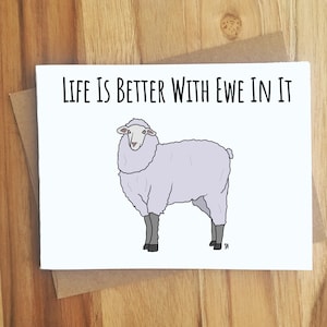 May include: A white card with the text "Life is better with ewe in it" and a cartoon illustration of a white sheep.