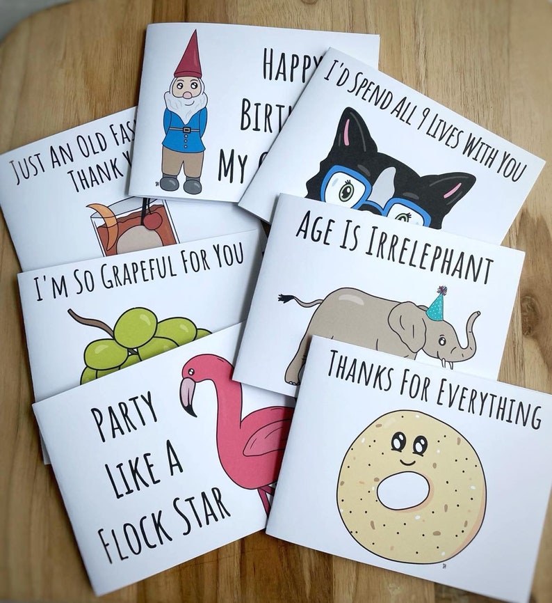K&ouml;nnte beinhalten: Ein Set mit zehn Gru&szlig;karten mit humorvollen Illustrationen und Text. Die Karten zeigen einen Gnom, eine Katze, einen Elefanten, einen Flamingo, einen Bagel und Trauben. Der Text auf den Karten enth&auml;lt S&auml;tze wie "Happy Birthday", "Ich bin so dankbar f&uuml;r dich" und "Alter ist irrelephant".