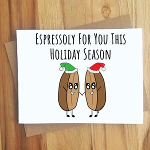 May include: A white greeting card with the text "Espressoly For You This Holiday Season." The card features two cartoon coffee beans holding hands, each wearing a Santa hat. The card is on a brown envelope.