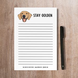 May include: A white lined notepad with a cartoon golden retriever dog and the text "STAY GOLDEN". The notepad has the text "BAD JOKES BY GOOD PEOPLE - WWW.SKPINK.COM - @SKP.INK" at the bottom.