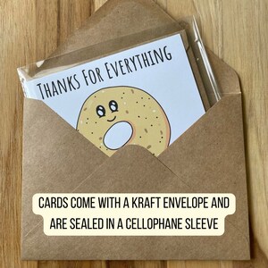 K&ouml;nnte beinhalten: Ein brauner Umschlag mit einer wei&szlig;en Karte darin. Die Karte zeigt ein Cartoon-Bagel mit einem l&auml;chelnden Gesicht und dem Text "THANKS FOR EVERYTHING". Der Umschlag und die Karte sind in einer Cellophanh&uuml;lle versiegelt.