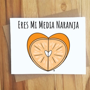 May include: A white card with the text "Eres mi media naranja" in black lettering. The card features a graphic of a heart-shaped orange slice with a small white heart in the center.