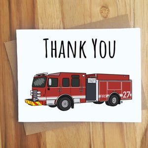 May include: A white card with the words "THANK YOU" in black lettering. Below the text is a red fire truck illustration with the number 27 on the side. The card is on a wooden surface.
