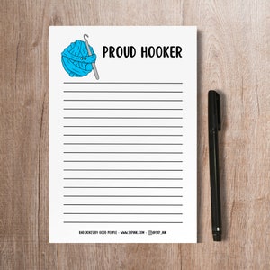 May include: A white printable notepad with a blue yarn ball and crochet hook illustration. The notepad has lined paper and the text "PROUD HOOKER" at the top. The bottom of the notepad has the text "BAD JOKES BY GOOD PEOPLE - WWW.SKPINK.COM - @SKP_INK".