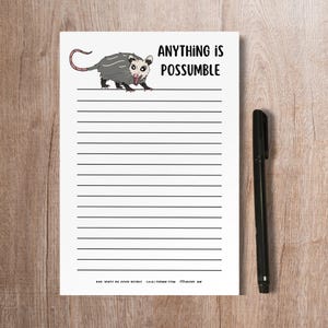May include: A white lined notepad with a black and white cartoon possum illustration and the text "Anything is Possumible".