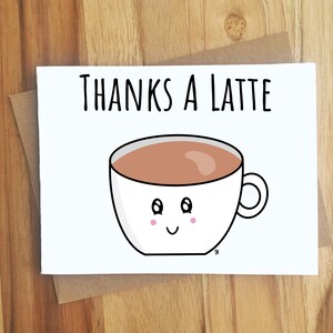 May include: A white greeting card with the text "THANKS A LATTE" above a cartoon coffee cup. The cup is white with a brown coffee filling, a handle, and a smiling face with pink cheeks. The card is inside a brown envelope.