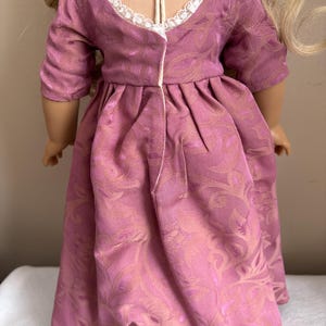 May include: A pink dress with a floral pattern and a white lace trim around the neckline. The dress has a gathered waist and a long skirt.