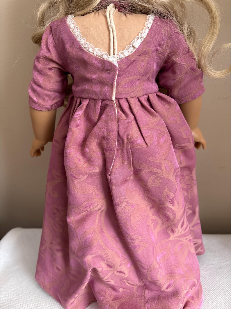 May include: A pink dress with a floral pattern and a white lace trim around the neckline. The dress has a gathered waist and a long skirt.