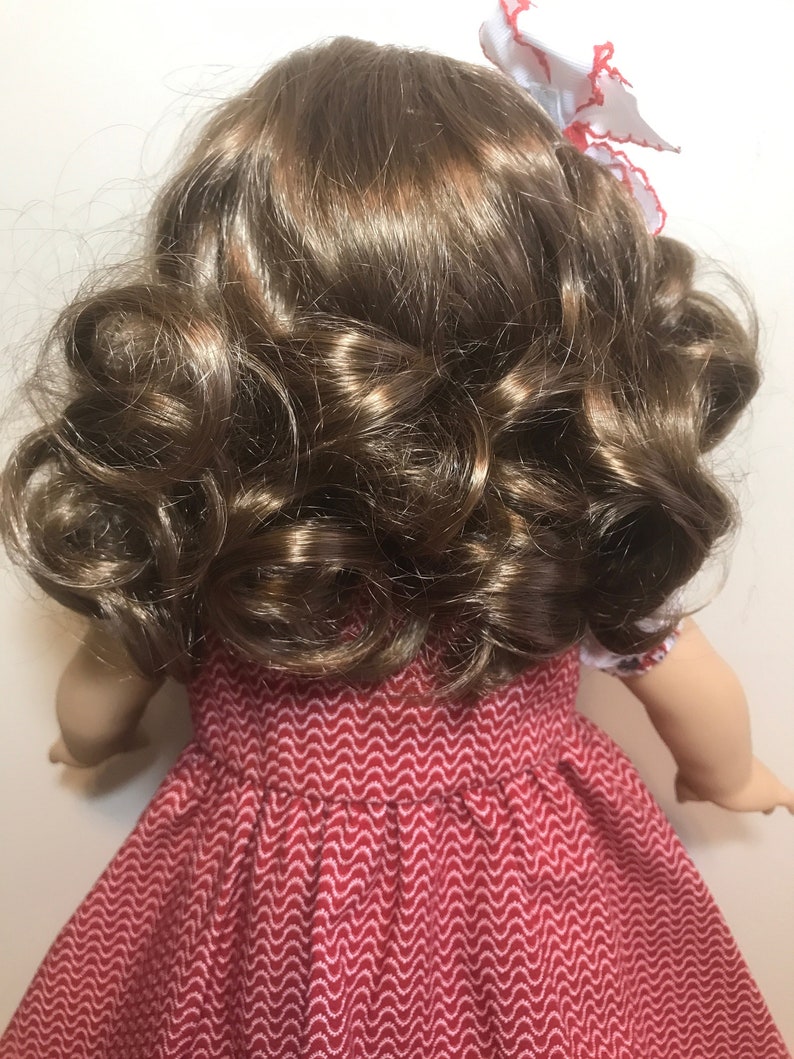May include: A doll with long, brown, curly hair. The doll is wearing a red dress with a white pattern.