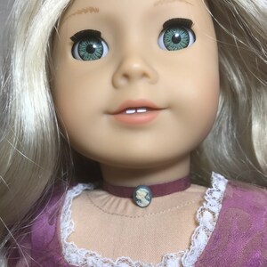 May include: A doll with blonde hair wearing a purple dress with white lace trim. The doll has green eyes and is wearing a dark red choker with a cameo pendant.