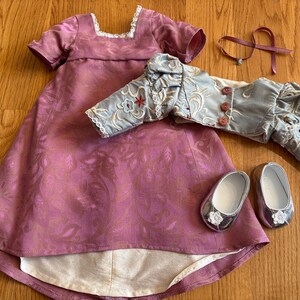 May include: A pink and white dress with a floral pattern, a light blue jacket with floral embroidery, and two silver shoes with white flowers.