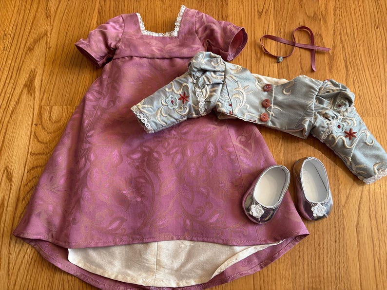 May include: A pink and white dress with a floral pattern, a light blue jacket with floral embroidery, and two silver shoes with white flowers.