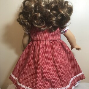 May include: A red dress with white trim and a white and red patterned underskirt. The dress has a scalloped hem and is made of a soft, cotton fabric. The dress is perfect for a doll.
