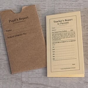 May include: A brown paper sleeve with a thumb notch labeled Pupil's Report with lines for Name and School District No. next to a cream-colored card titled Teacher's Report to Parents with fields for student details and a signature line.
