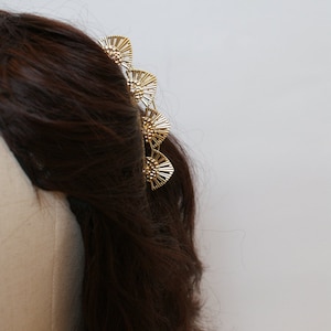 May include: A gold hair comb with a decorative design of overlapping fan shapes. The comb is worn in brown hair.