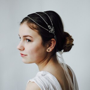 Può includere: Una donna con i capelli scuri indossa un abito bianco e una fascia per capelli in strass argentata con una catena pendente.