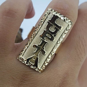 May include: Gold ring with a rectangular design featuring the word "JUGGL" engraved in bold letters.