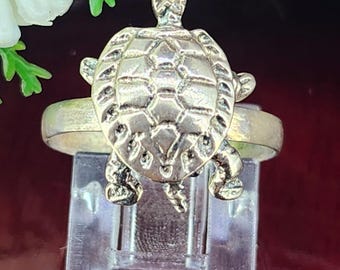 May include: A silver turtle ring with a detailed shell design. The ring is displayed on a clear plastic ring holder.