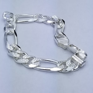 May include: A silver-colored Figaro chain bracelet. The bracelet features a pattern of three small circular links followed by one elongated oval link. The links have a textured, diamond-cut design. The clasp is a fold-over style.