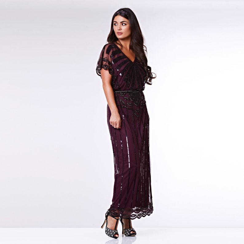 May include: A long, burgundy sequined dress with a V-neckline and short sleeves. The dress has a beaded belt and a flowing skirt.