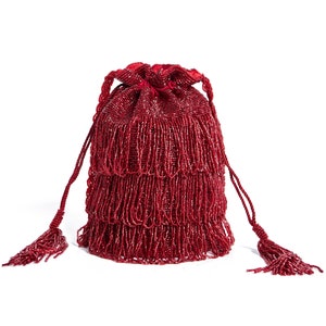 Può includere: Una borsa a cordoncino rossa con perline e fondo a frange. La borsa ha un fiocco su ogni lato.