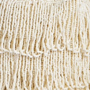 May include: A cream-colored handbag covered in layers of hanging beaded fringe. The surface is entirely composed of small, uniform, cylindrical beads arranged in vertical strands that create a textured, tiered appearance across the entire exterior.