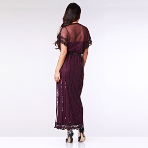 May include: A long, burgundy sequined dress with a sheer overlay and short sleeves. The dress has a fitted bodice and a flowing skirt.