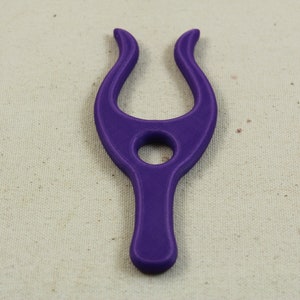 May include: A purple plastic tool with a unique shape, resembling a stylized letter Y. It has a hole in the center and two curved arms.