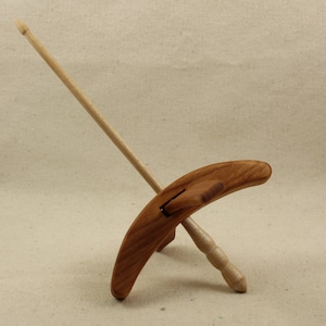Op de afbeelding: Een houten drop spindle voor hand spinnen. Het heeft een gebogen, peddelvormige wirtel van donkerder hout en een lange, dunne schacht. Deze traditionele tool wordt gebruikt om garen te creëren van vezels, een sleutelelement in textiel ambachten.