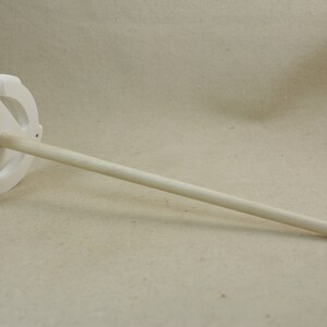 May include: White ceramic spinning wheel with a wooden spindle. The wheel has a circular design with three spokes.