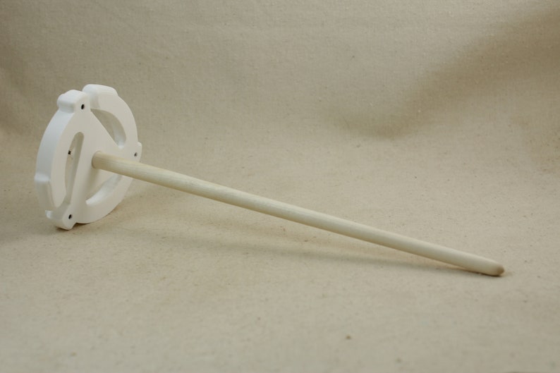 May include: White ceramic spinning wheel with a wooden spindle. The wheel has a circular design with three spokes.