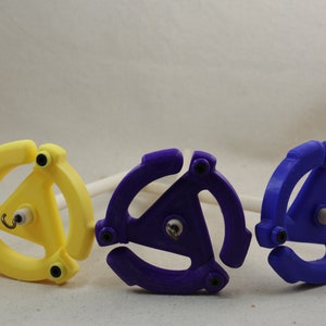 May include: Three spinning wheels for yarn, one yellow, one purple, and one blue. Each wheel has a three-pronged design and a small hook in the center.